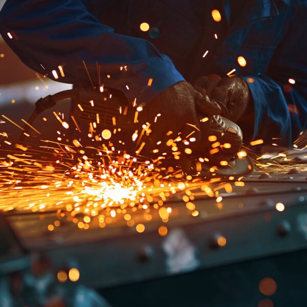 Close up of worker in special dark blue uniform working with equipment for metal near orange sparks in smithy. Concept of creating modern fence with special tools.