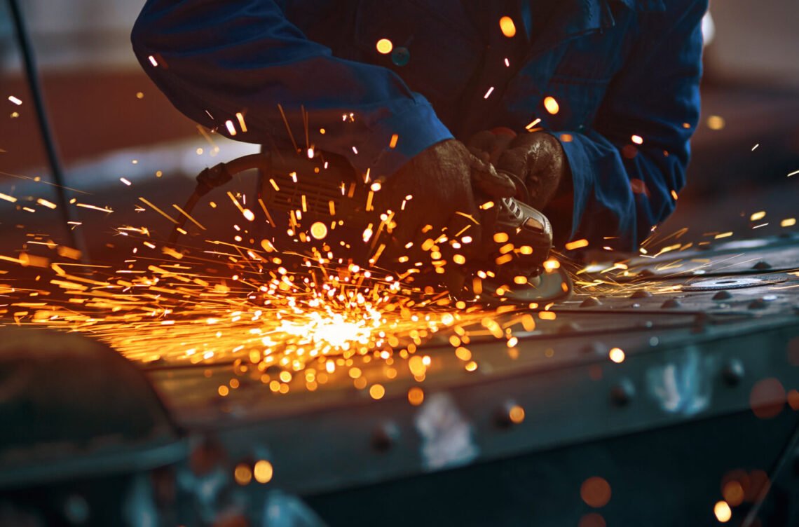 Close up of worker in special dark blue uniform working with equipment for metal near orange sparks in smithy. Concept of creating modern fence with special tools.