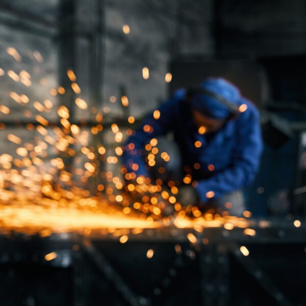 Close up of young man in blue special uniform doing gate by electric steel cutter machine for welding special metal. Concept of process produce modern fence in garage.